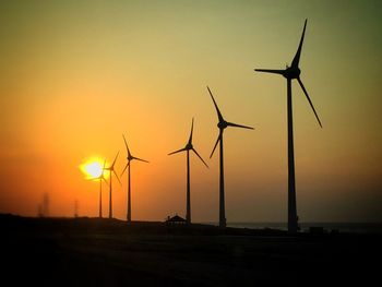 Low angle view of silhouette windmill on field against sky during sunset