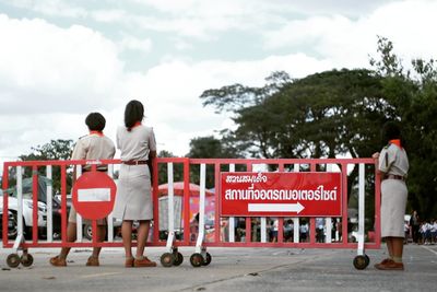 Rear view of women standing by red sign board against sky