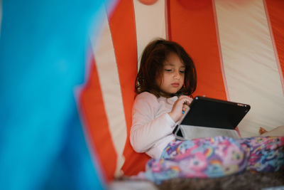 Four-year-old girl in pajamas looking at tablet in a little house