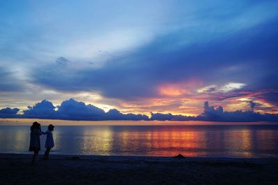 Silhouette people standing on beach against sky during sunset