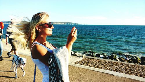 Side view of woman photographing while standing against sea