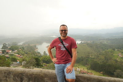 Portrait of smiling young man standing on mountain against sky