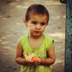 Cute boy holding fruit while standing on footpath