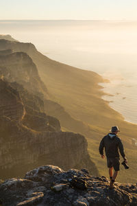 High angle view of man with camera walking on rocky mountains against sea