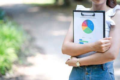 Midsection of businesswoman holding clipboard with data