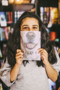 Portrait of girl showing book cover while standing in bookstore