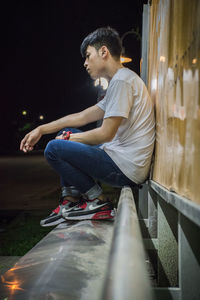 Side view of young man looking away while sitting against wall