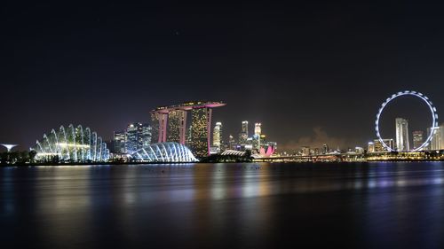 Illuminated city by sea against sky at night