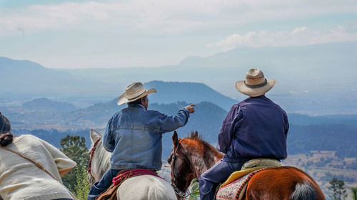 Rear view of people riding on mountain against sky