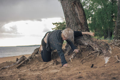 Young woman relaxing on sand at beach against sky