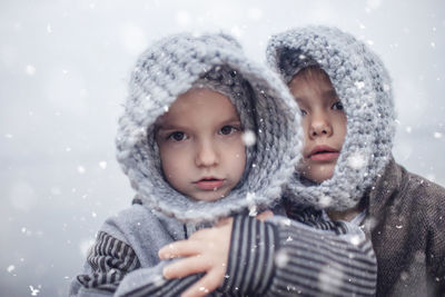 Girl in knitted grey hat hugging her frozen smaller brother