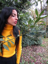 Young woman looking away while standing against trees