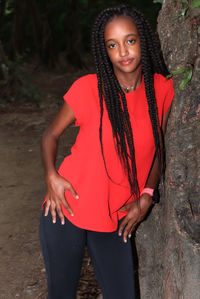 Portrait of young woman with braids standing against tree trunk