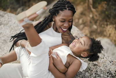 Merry african american mother with curly hair hugging and tickling happy daughter while spending summer weekend day in countryside together