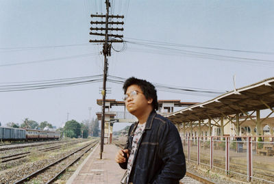 Young man using mobile phone by railroad tracks against sky