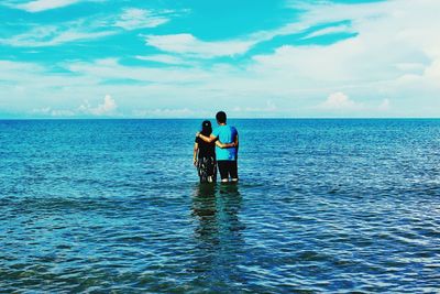 Rear view of couple standing in blue sea against sky