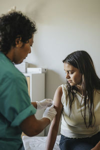 Mature doctor applying bandage on hand of young woman during vaccination in clinic