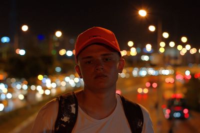 Portrait of young man standing against illuminated city at night