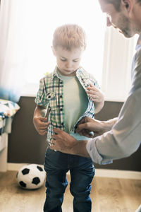 Father dressing up son at home on sunny day