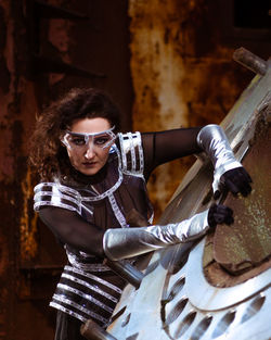 Strong woman in silver glasses and futuristic dress stands against the smoke in destroyed factory