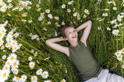Cheerful boy with hands behind head resting in flower field