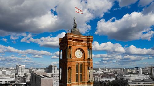 Clock tower amidst buildings in city against cloudy sky