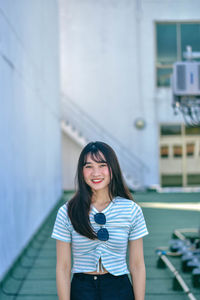 Portrait of smiling young woman standing on floor against building