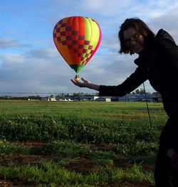 Optical illusion of smiling woman holding hot air balloon on field