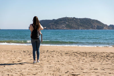 Rear view of woman standing at beach against sky