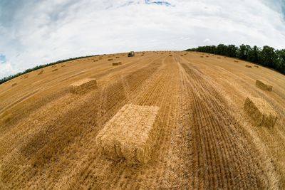 Fish-eye view of hay bales on field against sky