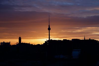 Silhouette of communications tower in city during sunset