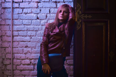 Portrait of young woman standing against brick wall