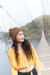 Young woman standing on bridge over river against sky