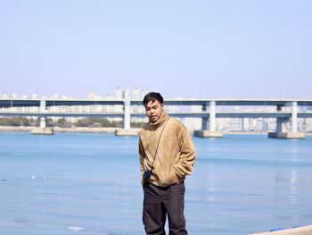 Portrait of young woman standing against river against clear sky