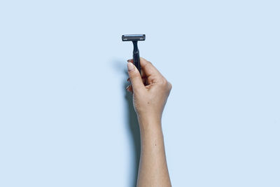 A person hand holds a multiple use shaving razor on blue background. view from above