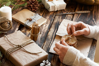 High angle view of woman makes trendy hand made gift package for christmas on wooden table. 