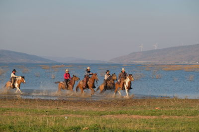 Group of people riding horse on field against sky