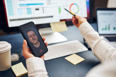 Woman entrepreneur having business video chat on smartphone with her business partner in office