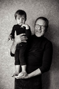 Grandfather with beard and glasses with his grandson sitting on his hands in the studio