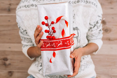 Midsection of woman holding christmas gift against wooden wall