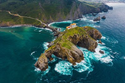 Drone view of paving stone way leading along stone bridge and ridge of rocky hill to lonely house on island gaztelugatxe surrounded by tranquil sea water under cloudy sky in basque country
