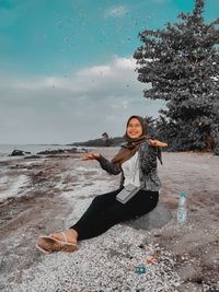 Portrait of young woman sitting on land against sky