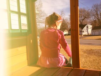 Rear view of girl sitting at porch on sunny day
