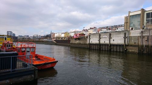 Boats moored in river against sky in city