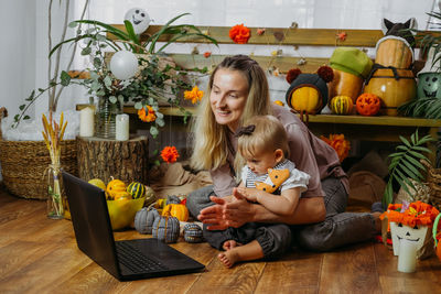 Mother with daughter clapping while sitting in front of laptop on floor at home