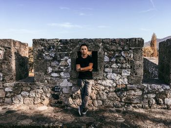 Full length of young man standing against stone wall