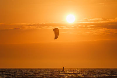 Silhouette man standing on sea against orange sky during sunset