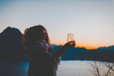 Woman holding illuminated lights against sky