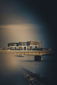 Illuminated buildings by river against sky at day