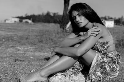 Portrait of young woman sitting on grassy field during sunny day